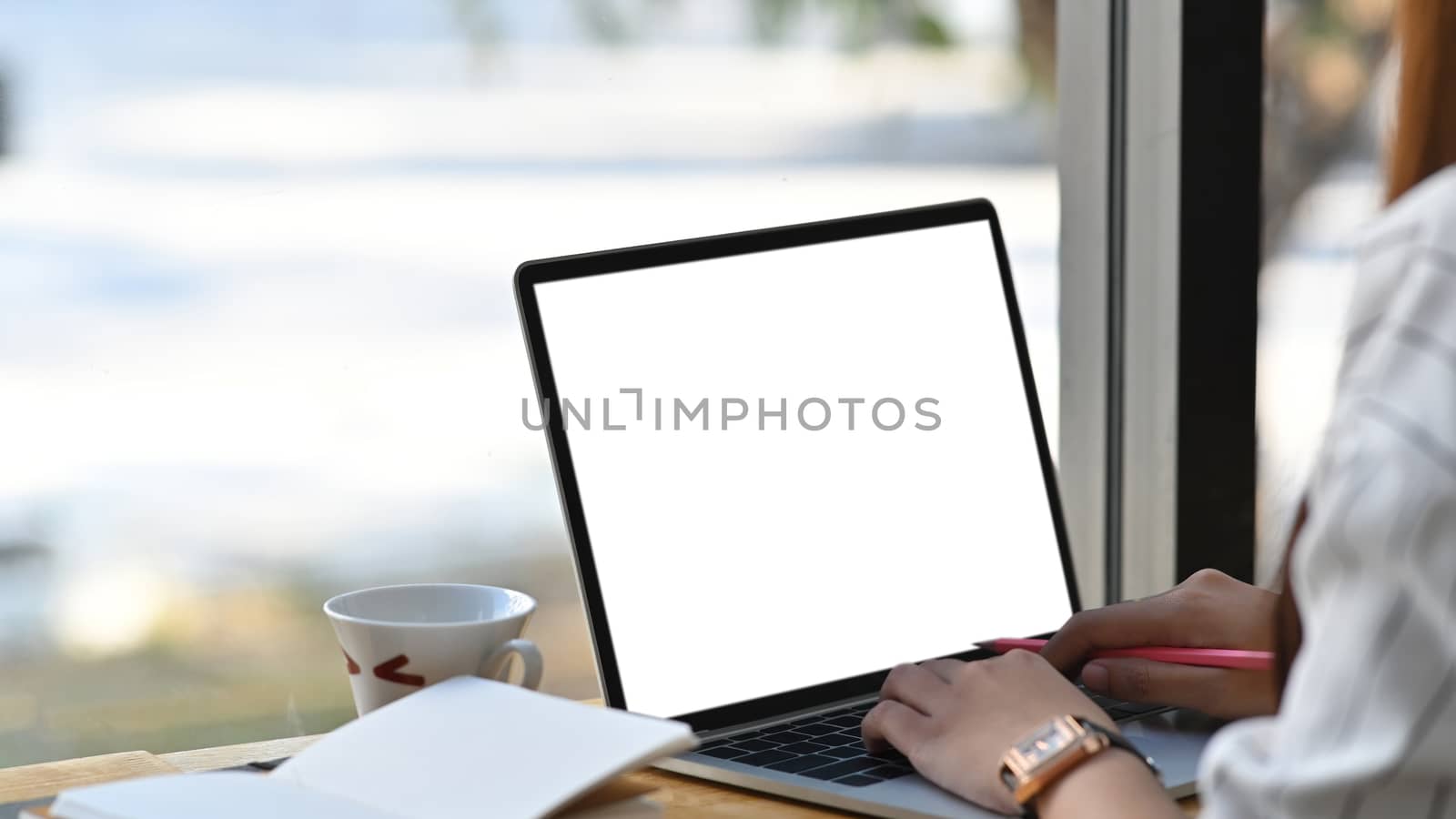 Close-up image of beautiful business woman sitting at the wooden work desk and typing on the white blank screen laptop keyboard.