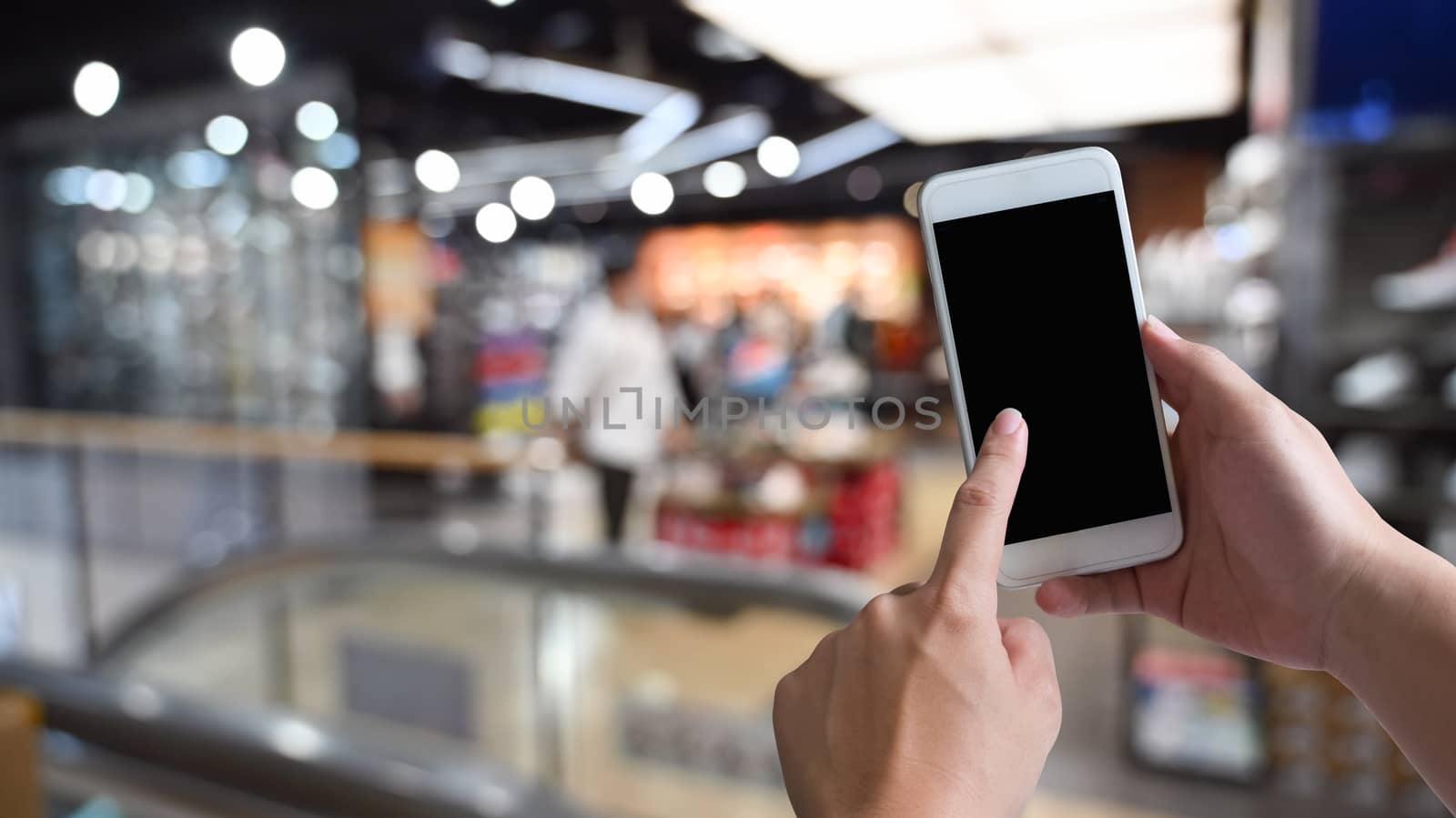 Close-up image of male hands using black blank screen smartphone at shopping center. Searching or social networks concept, Blurred background .