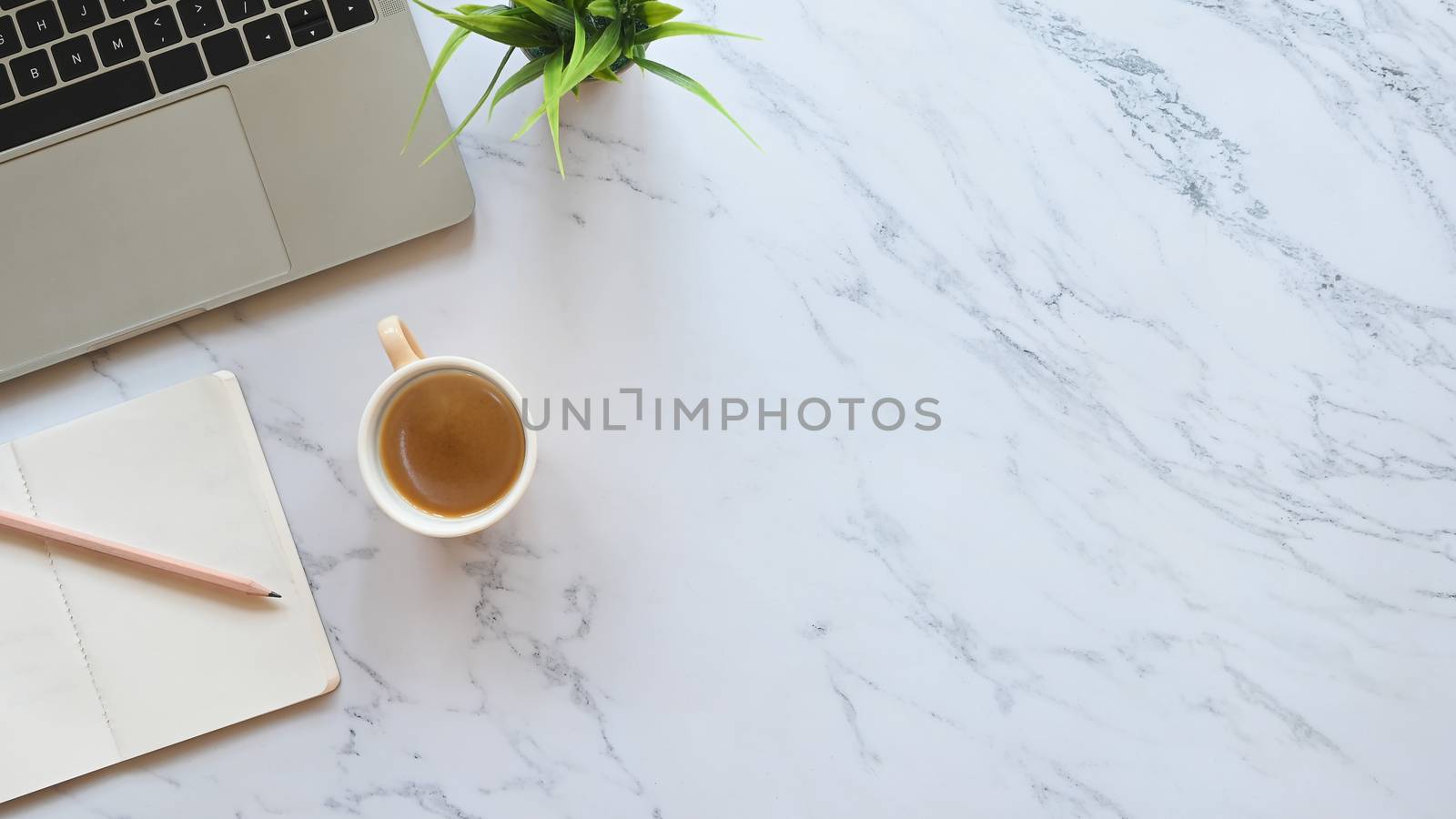 Close-up image part of laptop including coffee cup, pencil, notebook and potted plant putting on marble office table.