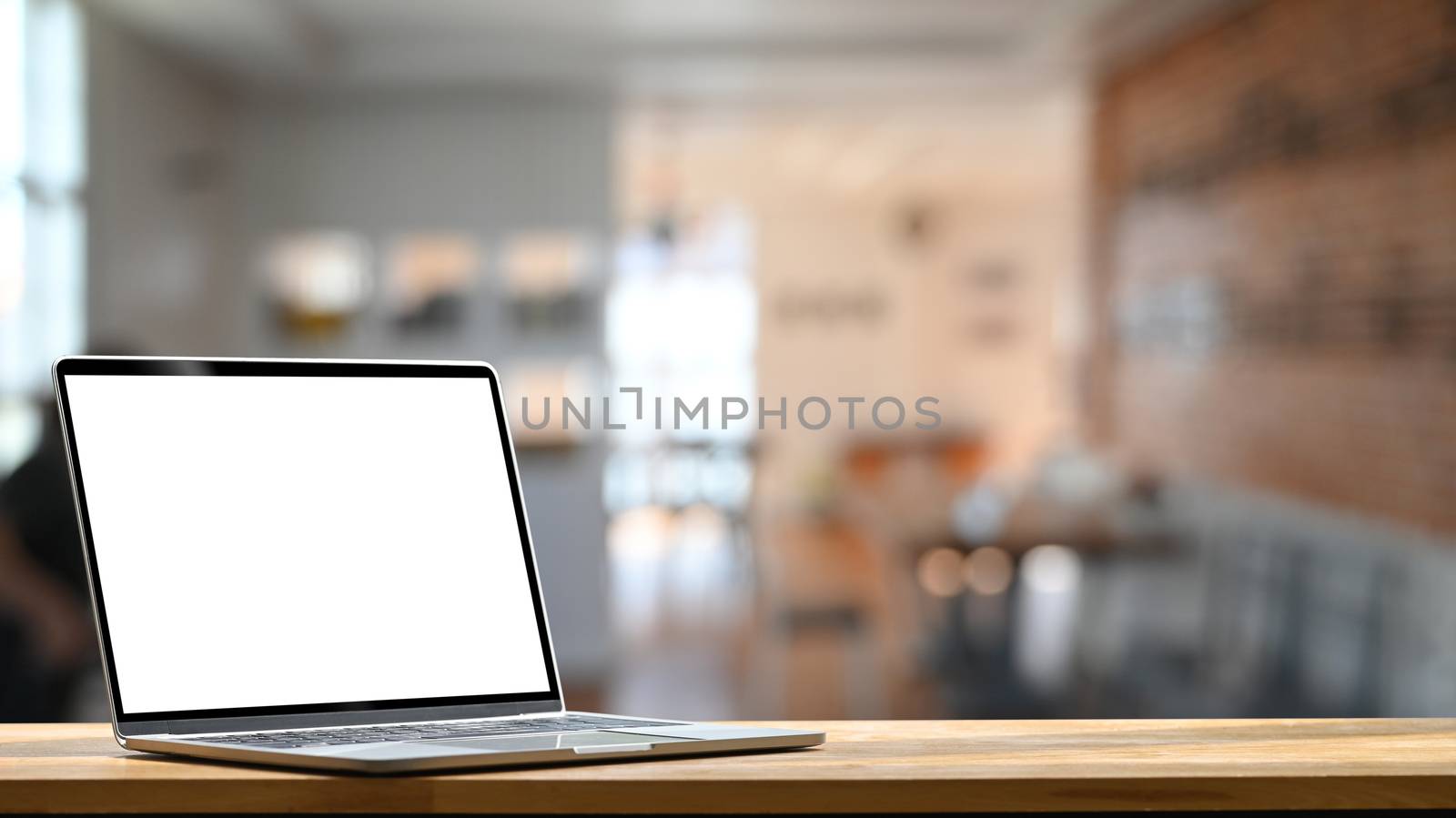 Photo of modern laptop with white blank screen display setting on the wooden table over the blurred modern room.