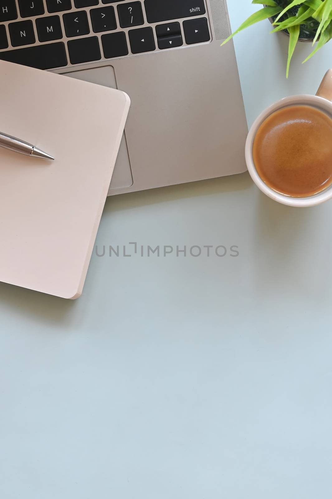 Office desk of laptop including coffee cup, pencil, notebook and potted plant putting on marble table.