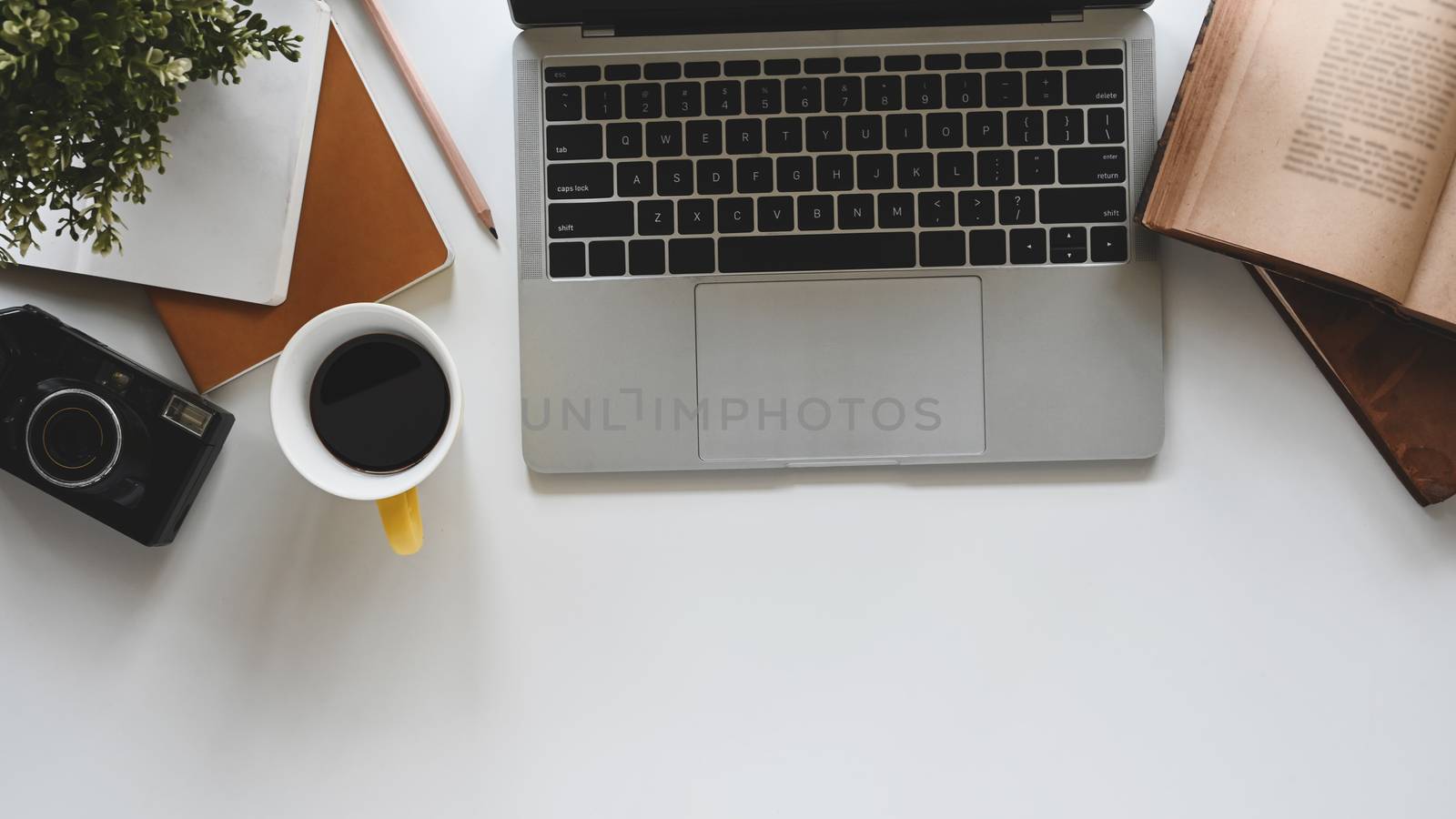 Modern office desk include laptop, camera, coffee cup, notebook, book, potted plant and pencil. Top view of office desk and office equipment.