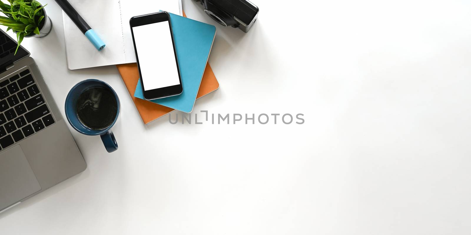 Modern office desk include laptop, camera, coffee cup, notebook, book, potted plant and pencil. Top view of white blank screen smartphone and Panorama banner background with copy space.