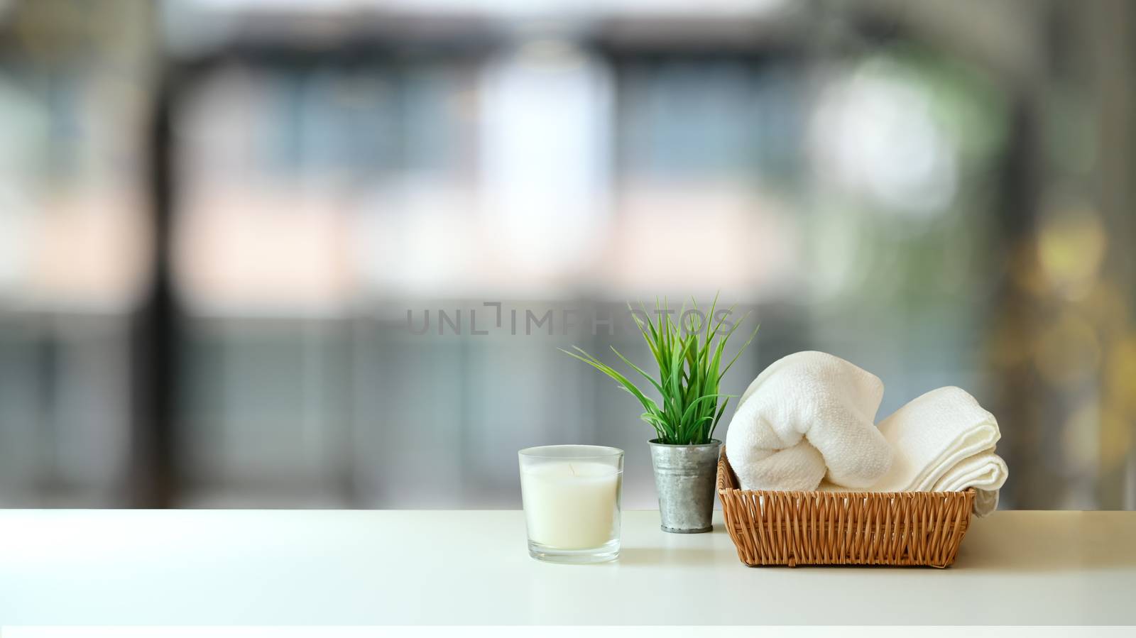 Towel is putting on the 
wicker basket, Candle and potted plant on the white table. Massage therapy concept.