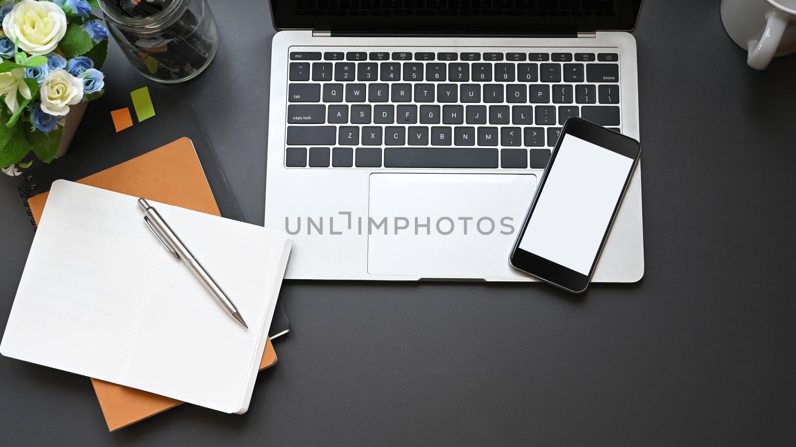 Top view office equipment such as laptop, white blank smartphone, notebook, pen, coffee cup and potted plant putting on modern working desk. Comfortable modern working desk concept.