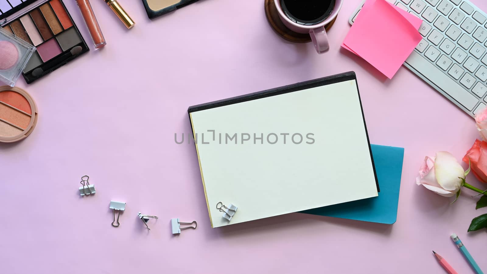 Top view image of feminine working desk including coffee cup, modern keyboard, notebook, pencil, bouquet and cosmetics putting on it. Women's working desk concept.