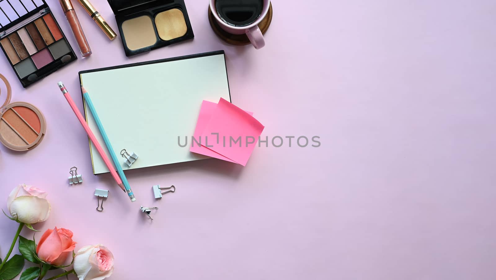 Top view of woman accessories putting on the pink working desk, including keyboard, coffee cup, bouquet, notebook, pen, women cosmetics and paper clip. Feminine working desk concept.