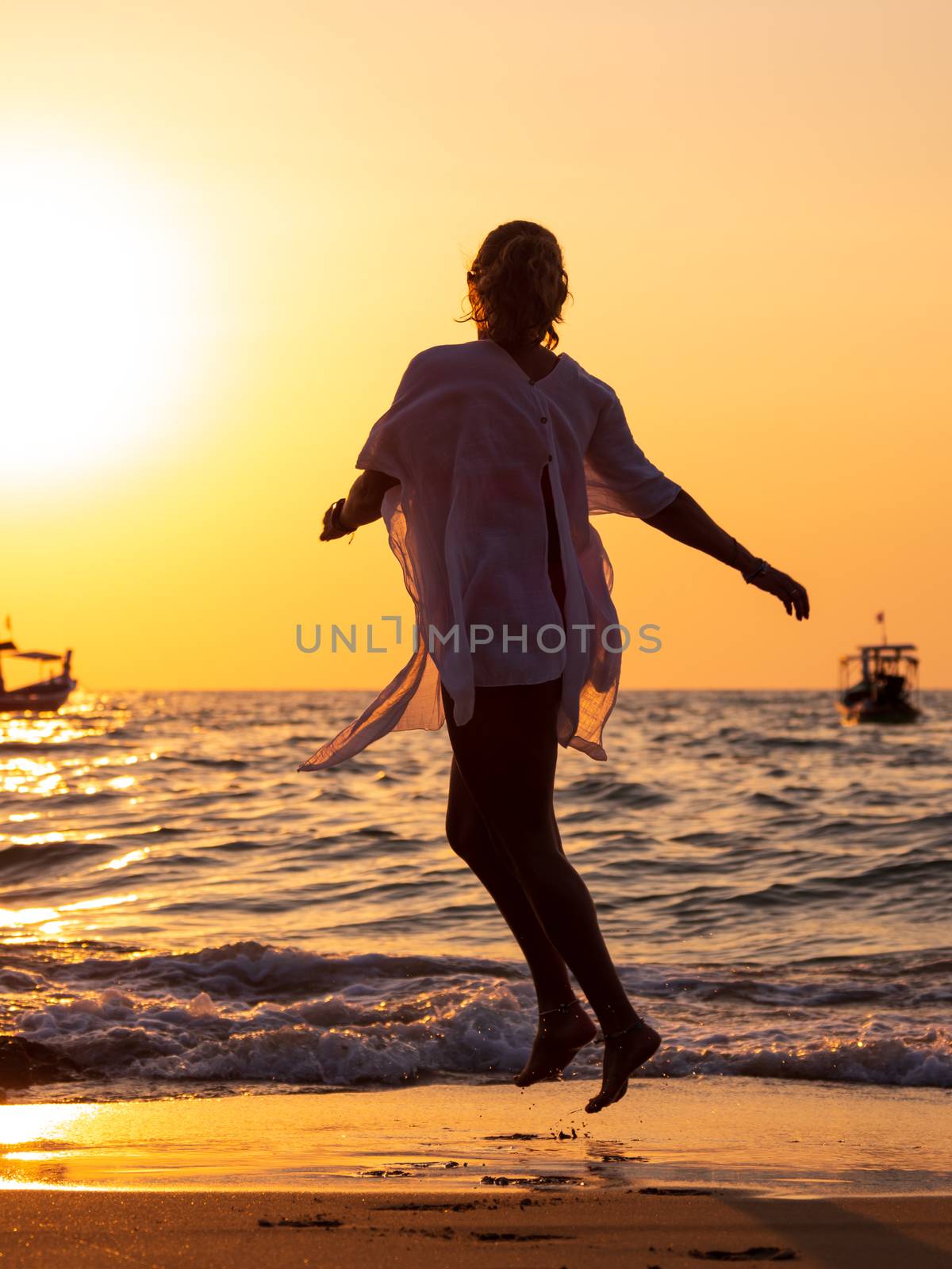 Silhouette of a young woman walking in the sea at sunset