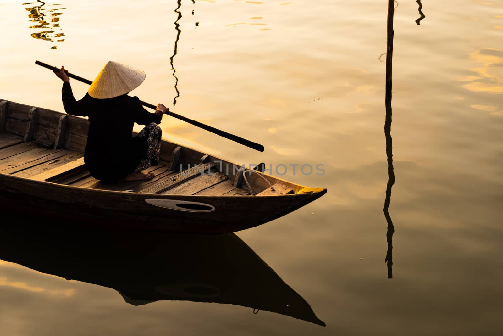 Vietnamese woman in traditional bamboo hat rowing on the Thu Bon River in evening