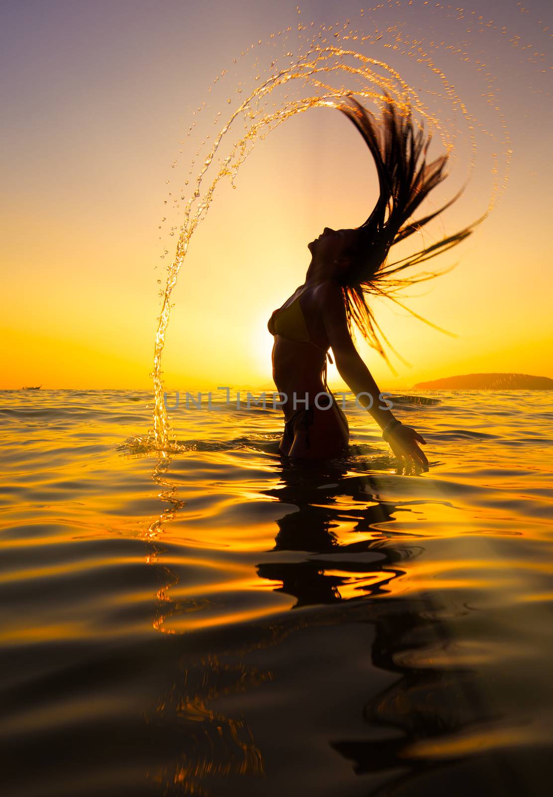 Woman in the sea at sunset flipping her hair out of the water