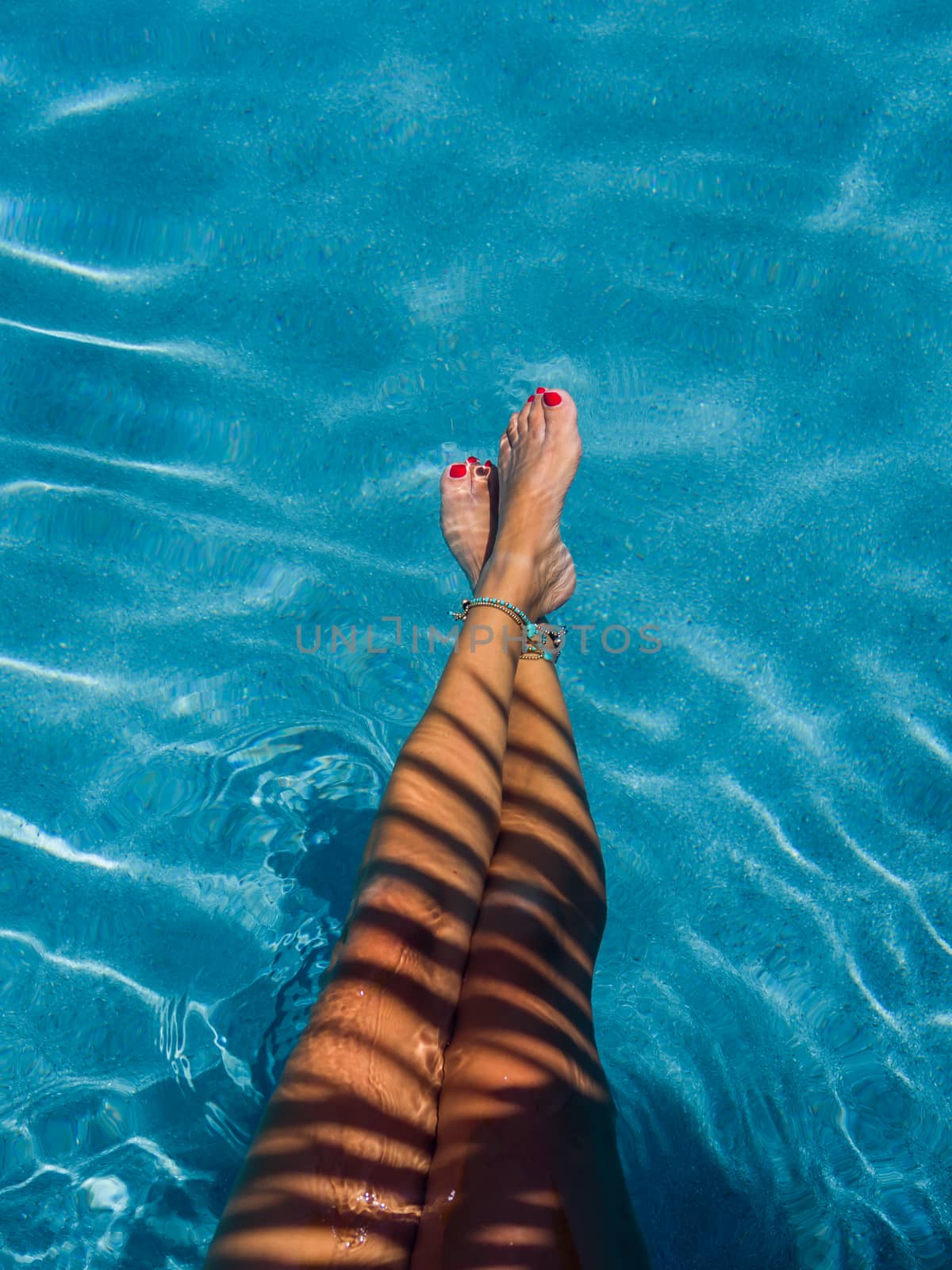 Woman relaxing in swimming pool at spa resort with the shadow of a coconut tree on her legs.