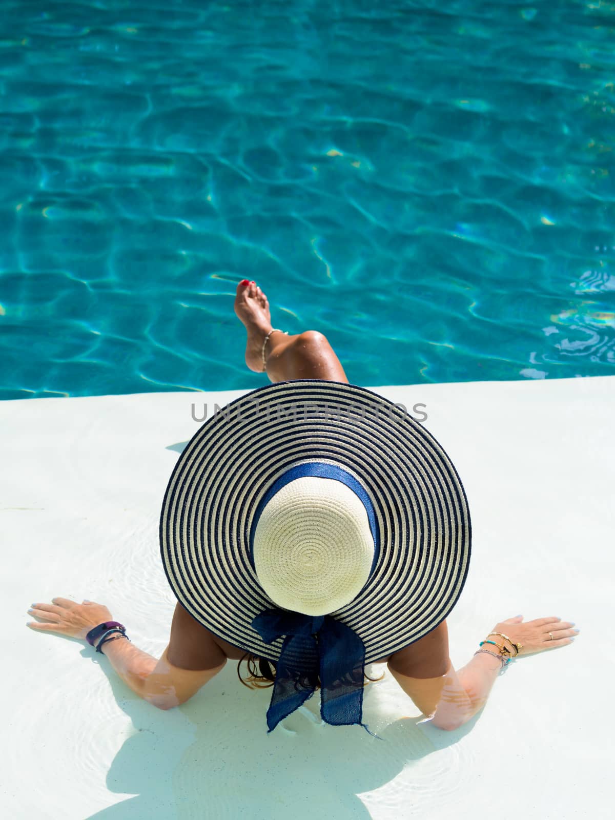 Woman wearing a straw hat sitting in the swimming pool at the luxury resort 