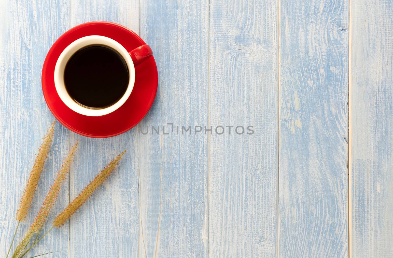 The grass flowers and red cup coffee on a wooden floor have a blue wooden floor as background.