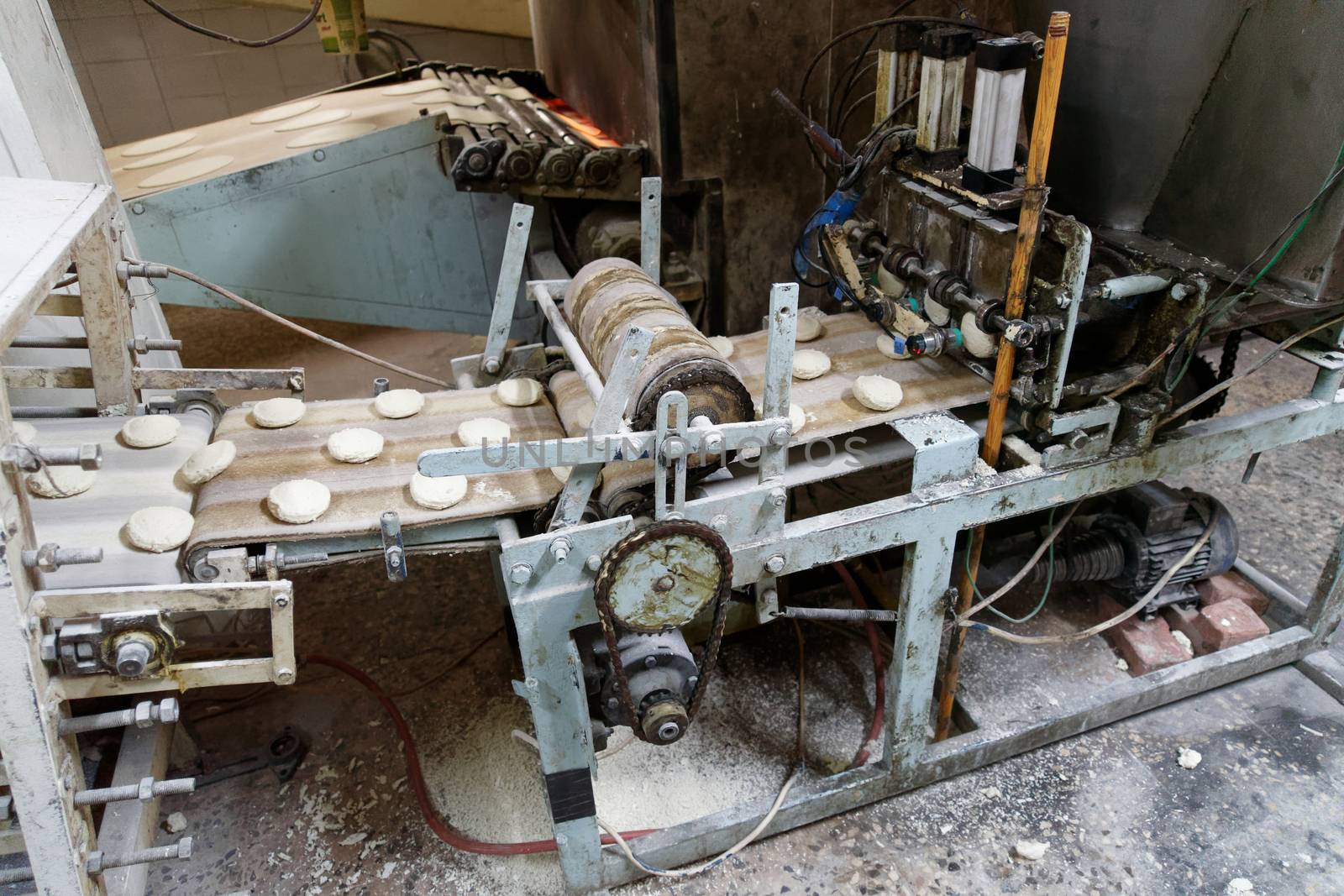 Old machine for forming dough pieces on a conveyor belt for the production of Arab flatbread in a large bakery in Aqaba, Jordan, middle east