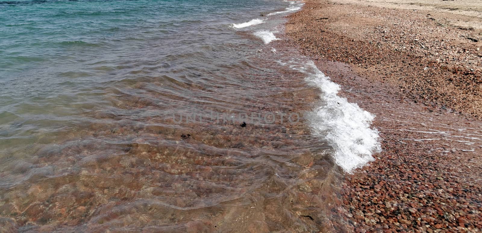 Small breaking wave at the beach of Aqaba in Jordan, covered with coarse gravel, middle east