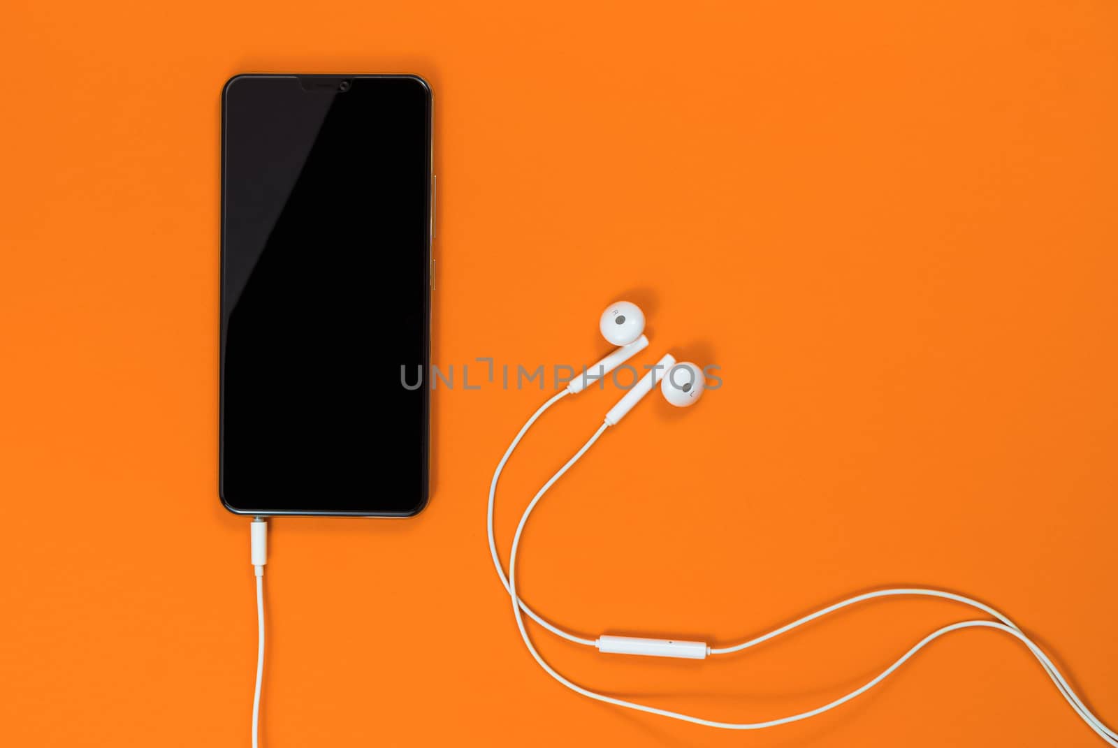 Close-up of smart phone with Earphones on a Orange background. (Top view). Listen to music.