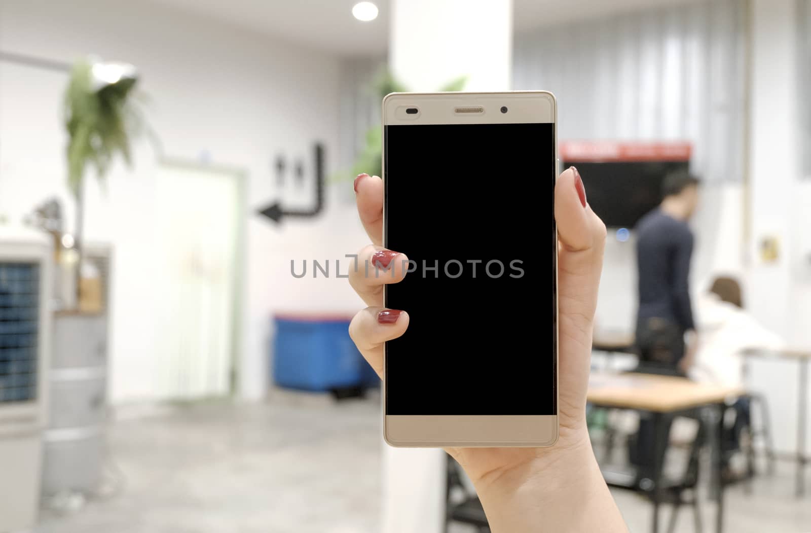 Woman hand holding the phone on Blurry Restaurant background by noomubon