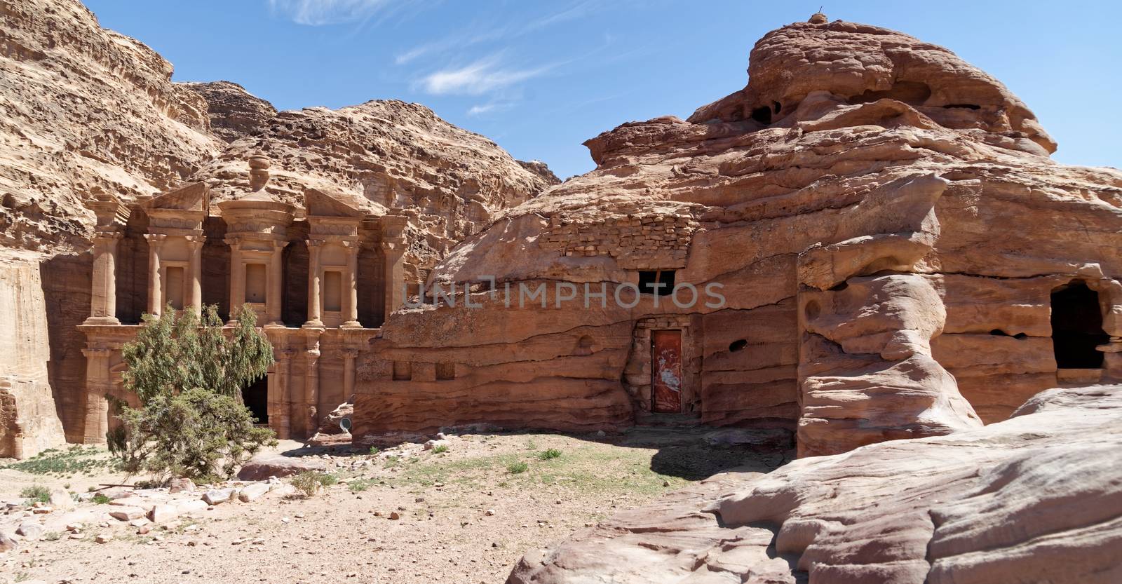 Cave dwelling, which is still used today as a storage room and recreation room, with Al-Deir Monastery in the background in the mountains of Petra, Jordan. by geogif