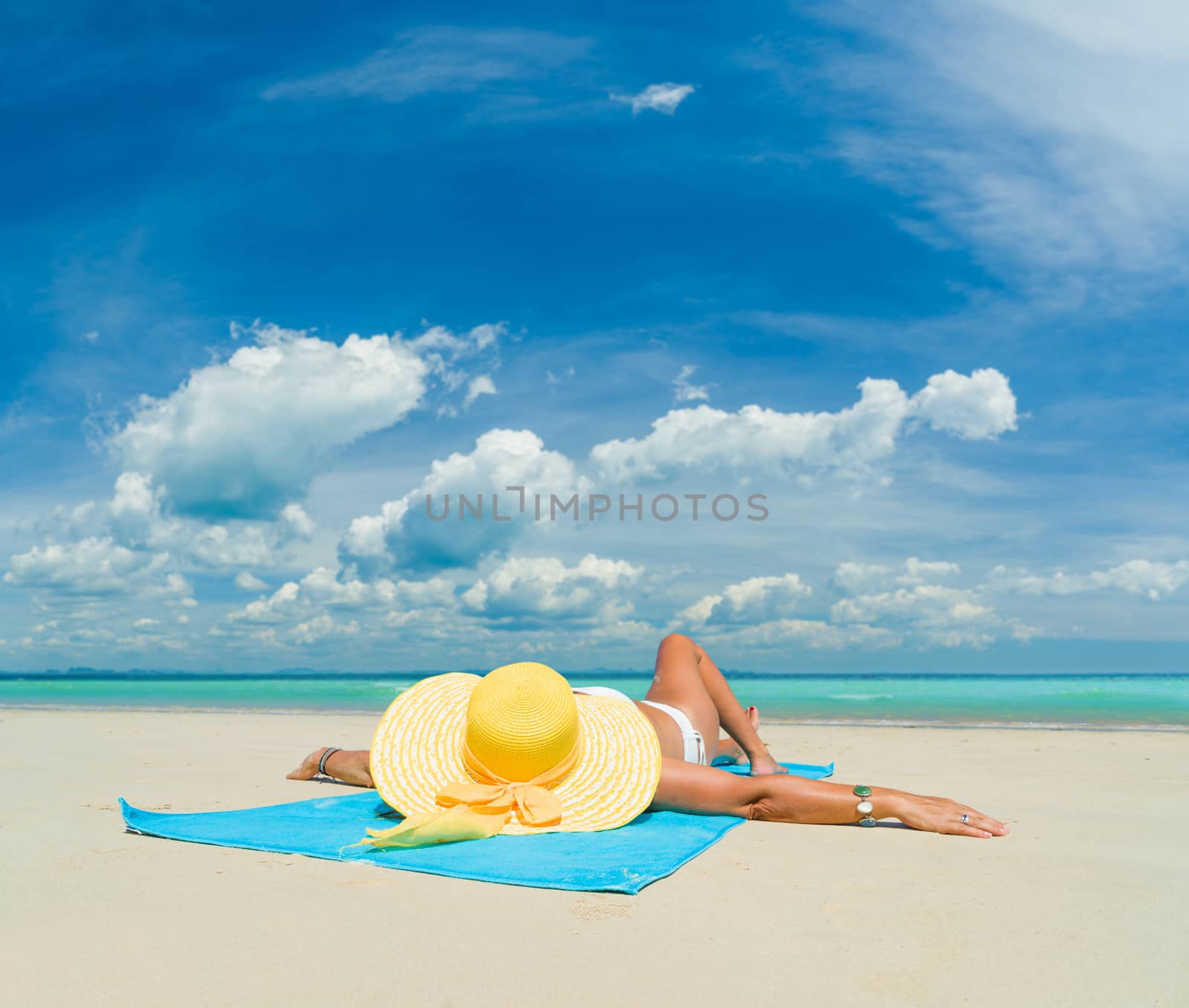 Woman in bikini wearing a yellow hat suntanning at tropical beach