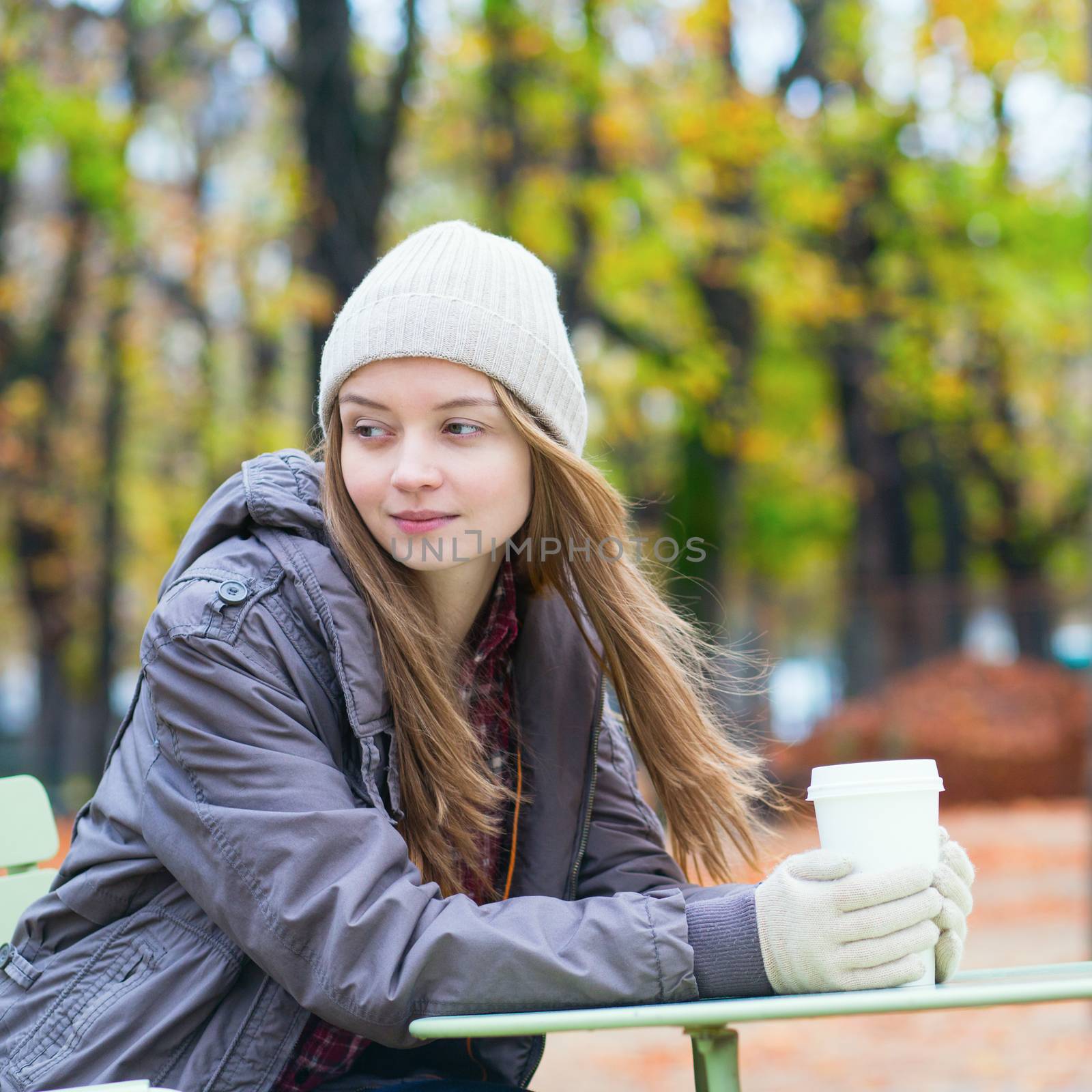 Young Parisian girl drinking coffee in the Luxembourg garden on a fall day