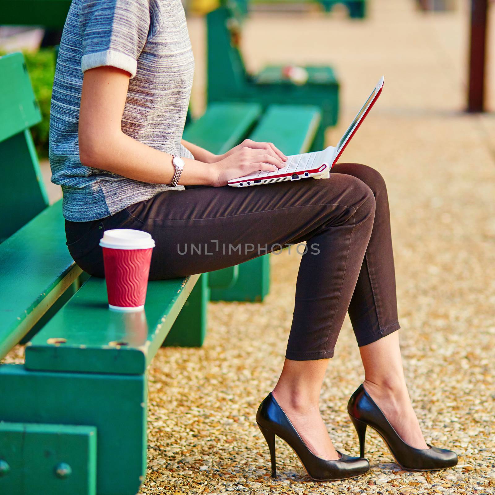 Young beautiful business woman drinking coffee and working on her laptop outdoors 
