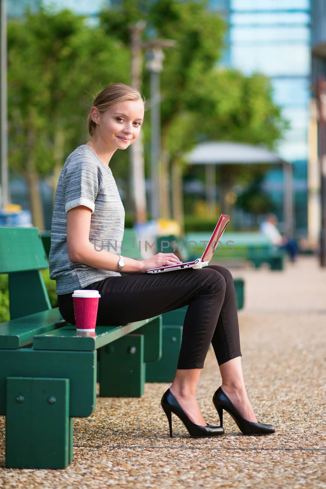 Young beautiful business woman drinking coffee and working on her laptop outdoors