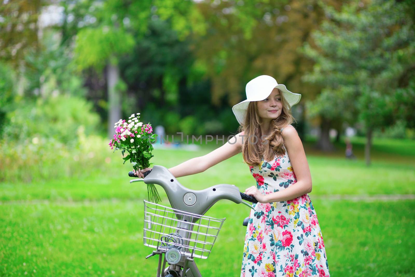 Happy young girl with bicycle and flowers in countryside on a summer day