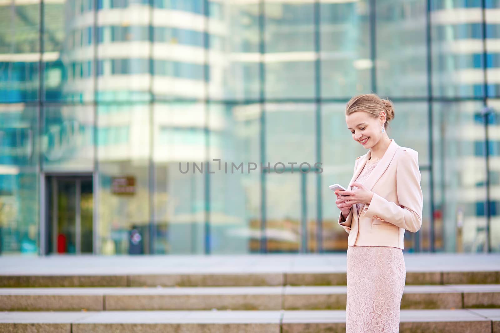 Young confident business woman in modern glass office interior using the mobile phone