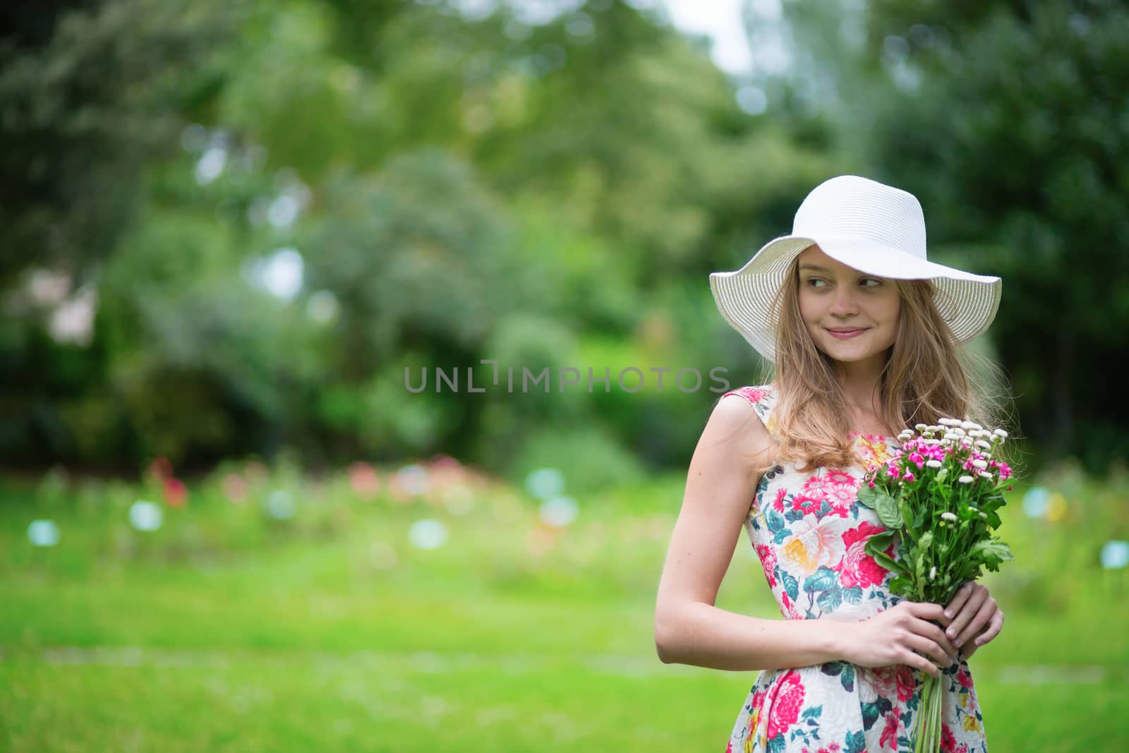 Beautiful young girl in white hat holding flowers