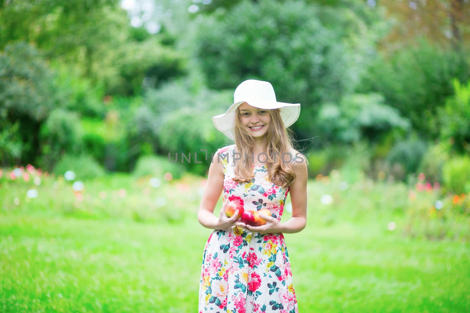 Beautiful young girl in white hat holding apples