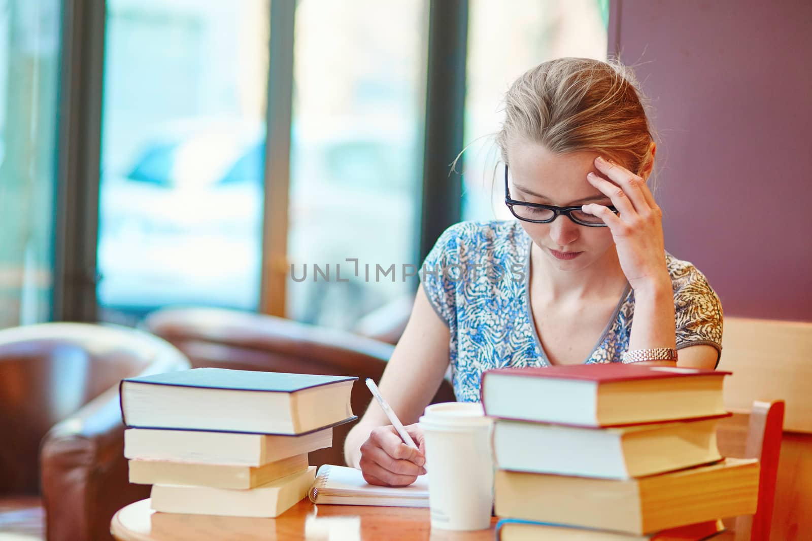 Beautiful young student with lots of books, studying or preparing for exams in a cafe. Shallow DOF