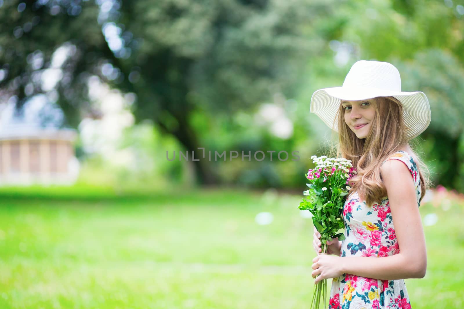 Beautiful young girl in white hat holding flowers