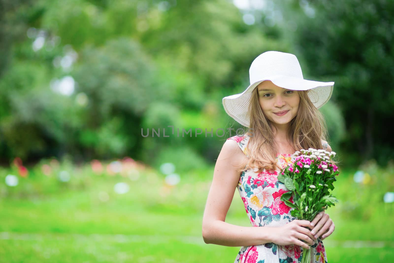 Beautiful young girl in white hat holding flowers