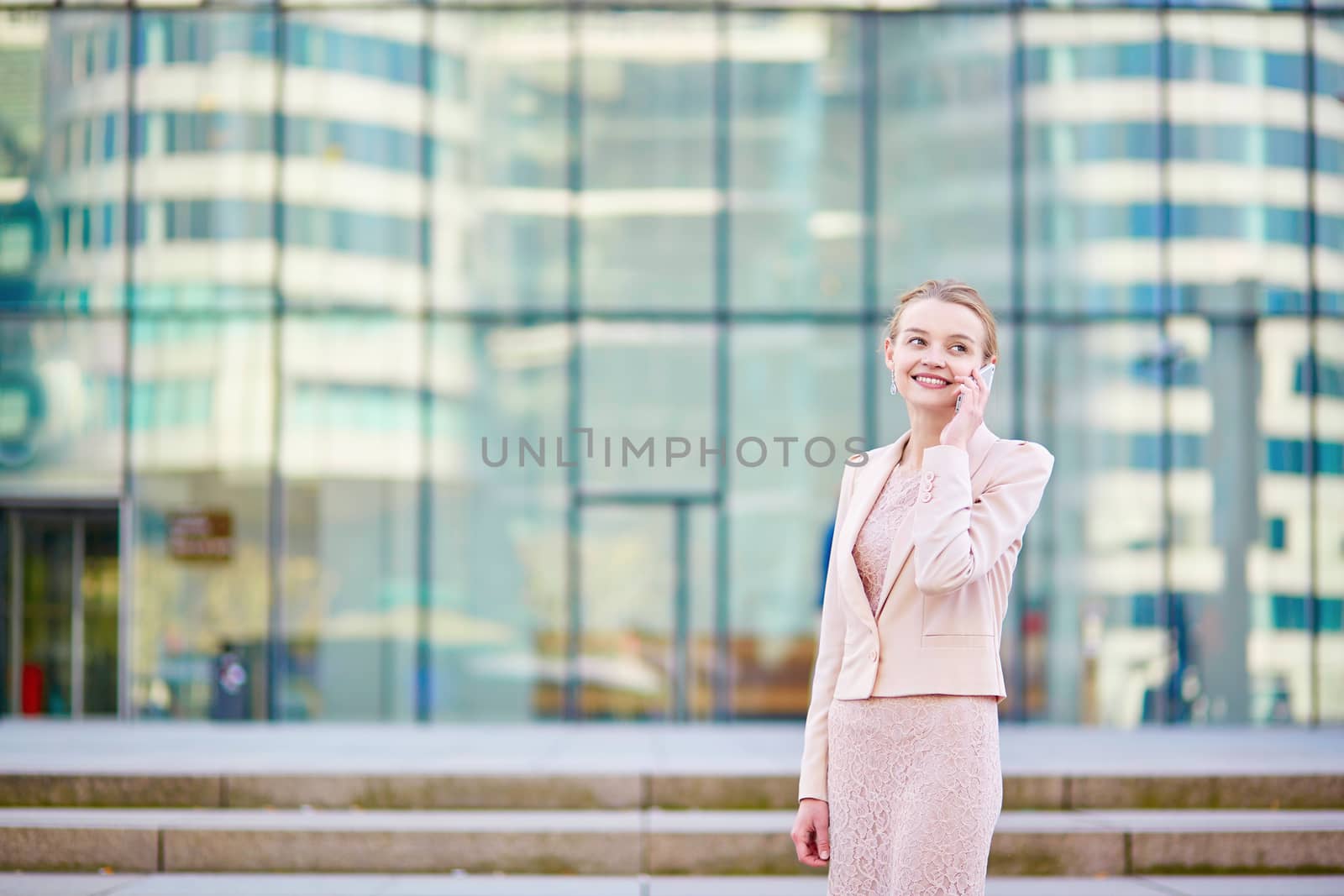 Young confident business woman in modern glass office interior  speaking on the mobile phone