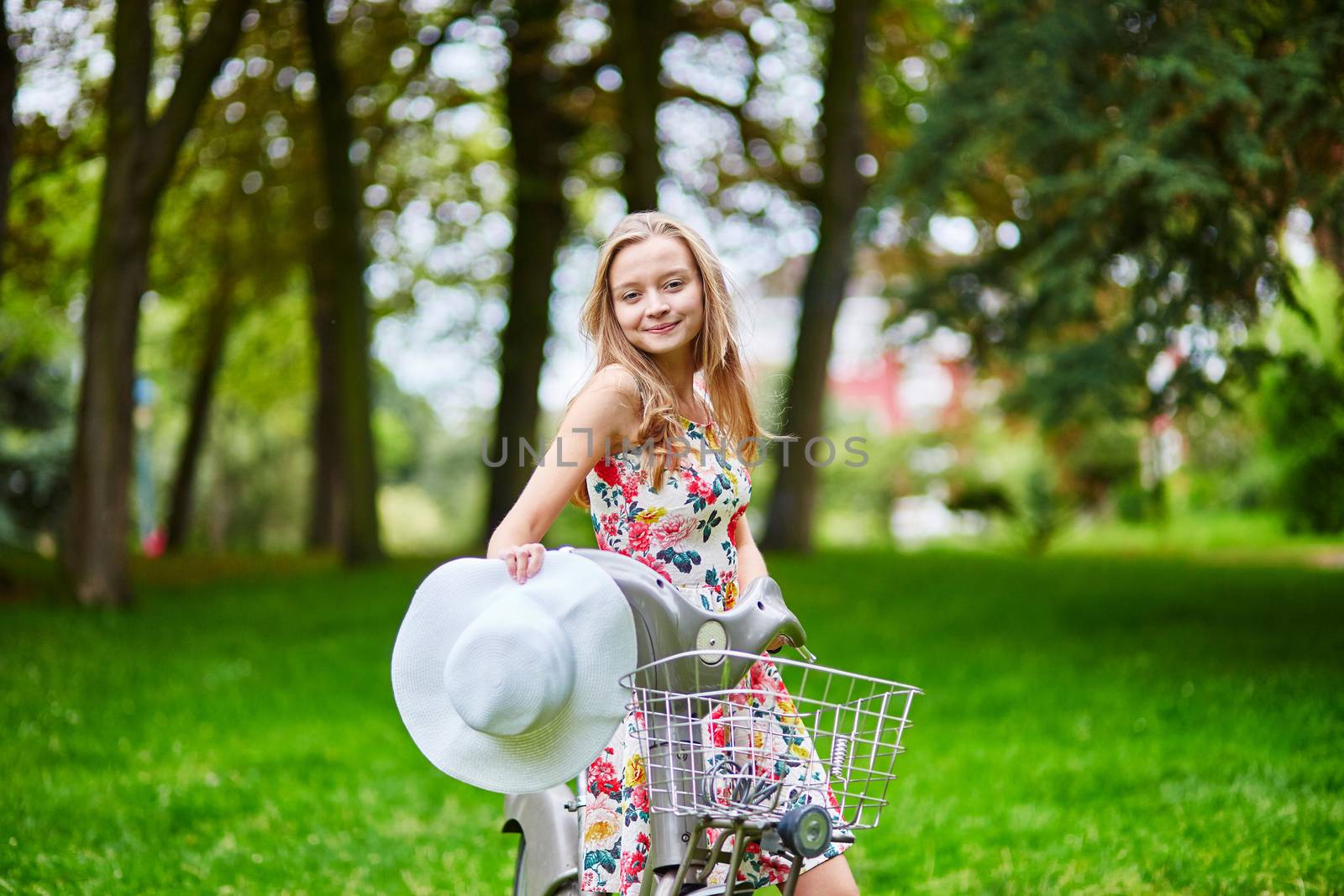 Happy young girl with bicycle and flowers in countryside on a summer day
