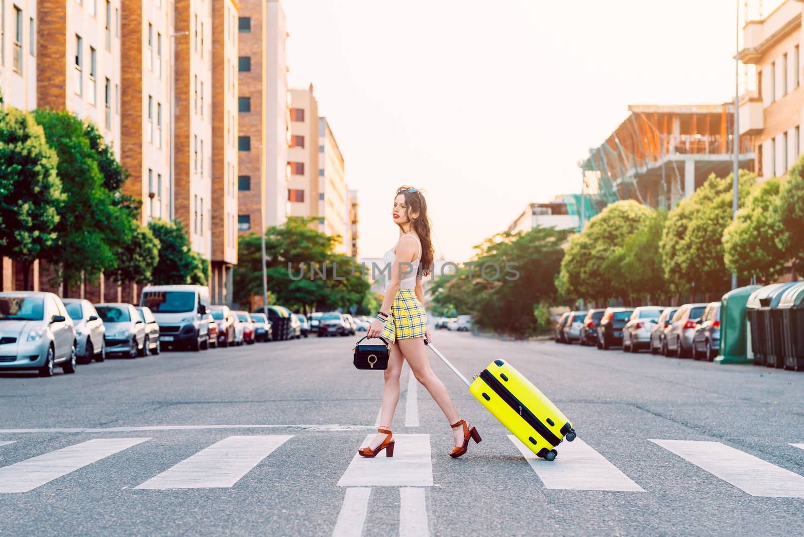 Young woman across the street with a yellow suitcase by Fotoeventis