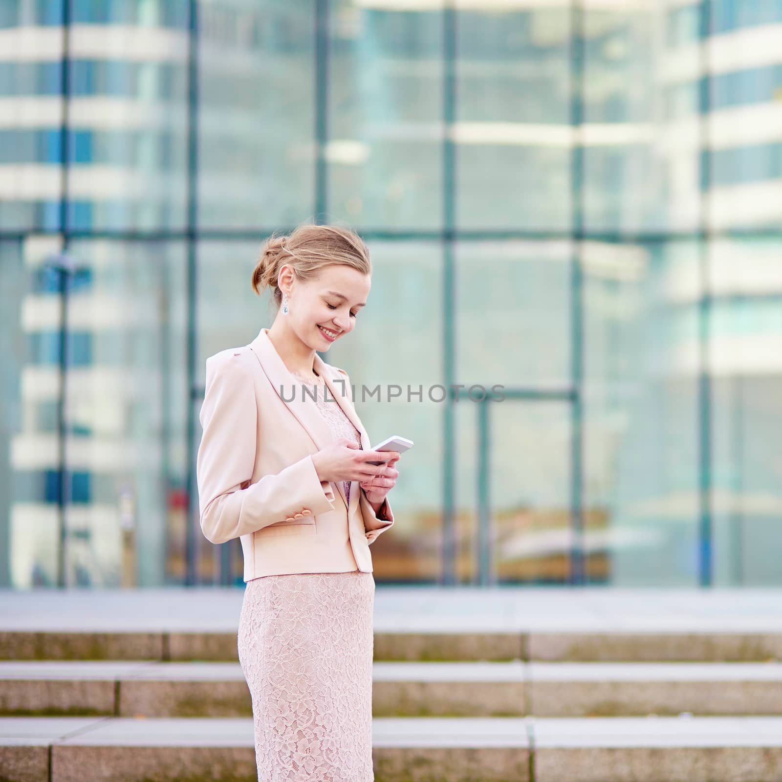 Young confident business woman in modern glass office interior using the mobile phone