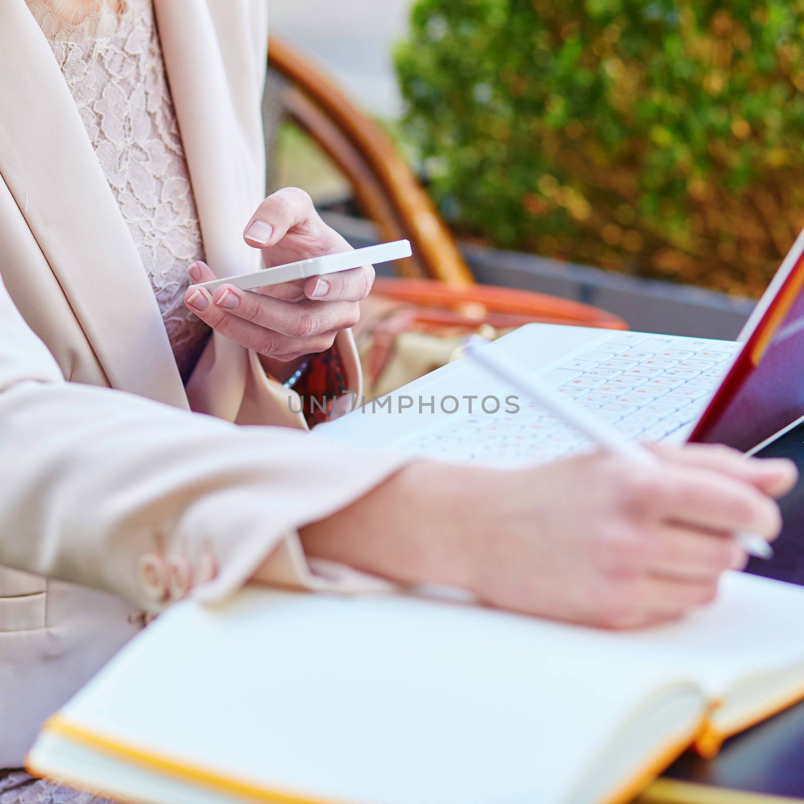 Business woman working in a cafe, writing something in her notebook and using mobile phone