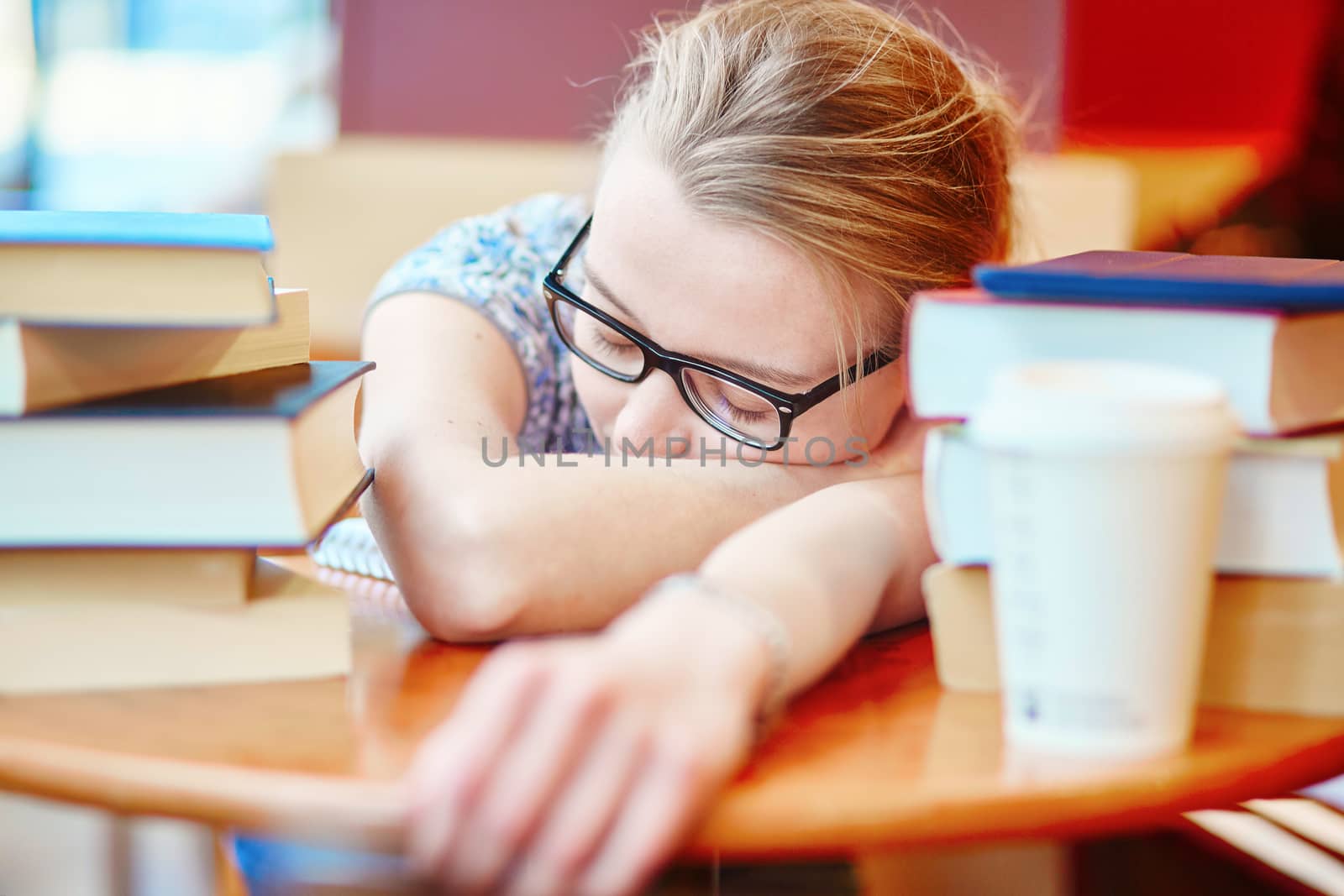 Beautiful young student with lots of books, sleeping on the table, tired of preparing for exams. Shallow DOF