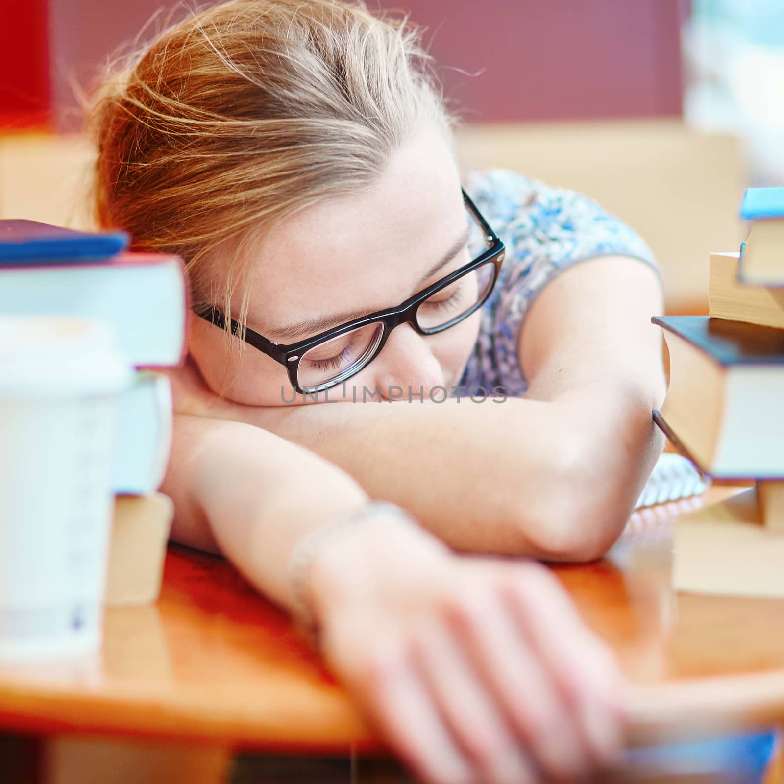 Beautiful young student with lots of books, sleeping on the table, tired of preparing for exams. Shallow DOF