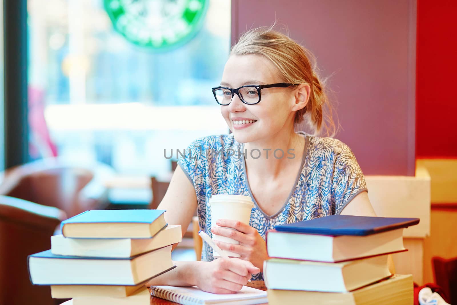 Beautiful young student with lots of books, studying or preparing for exams in a cafe. Shallow DOF