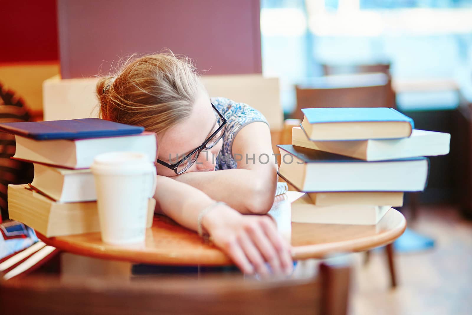 Beautiful young student with lots of books, preparing for exams in a cafe and sleeping on the table tired. Shallow DOF