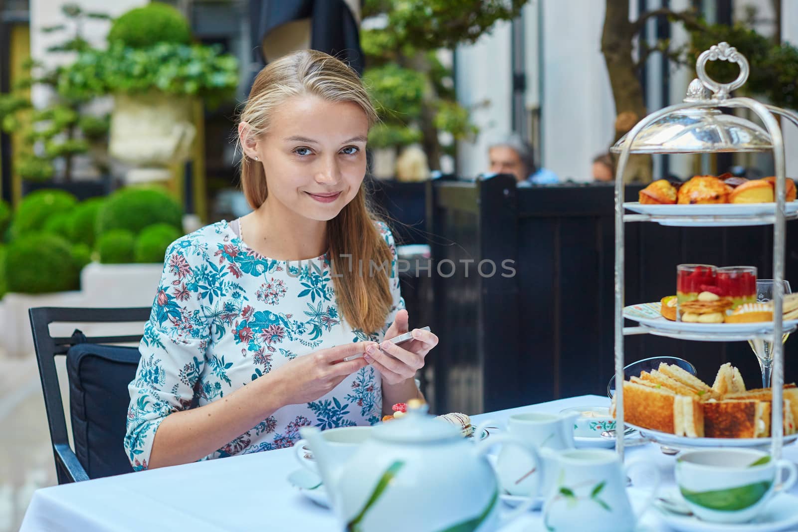 Beautiful young woman enjoying afternoon tea with selection of fancy cakes and sandwiches in a luxury Parisian restaurant