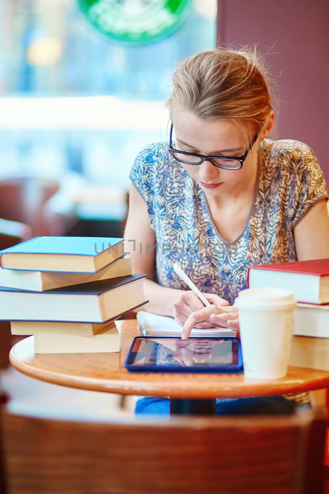 Beautiful young student with lots of books, studying or preparing for exams in a cafe. Shallow DOF