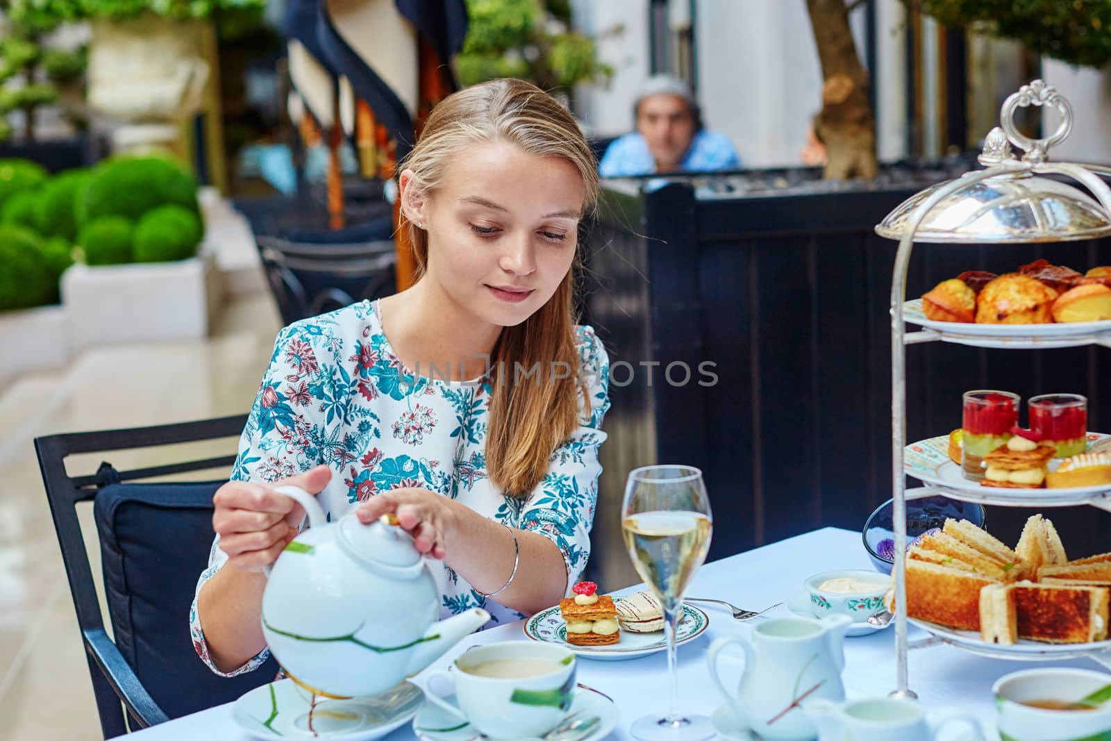 Beautiful young woman enjoying afternoon tea with selection of fancy cakes and sandwiches in a luxury Parisian restaurant