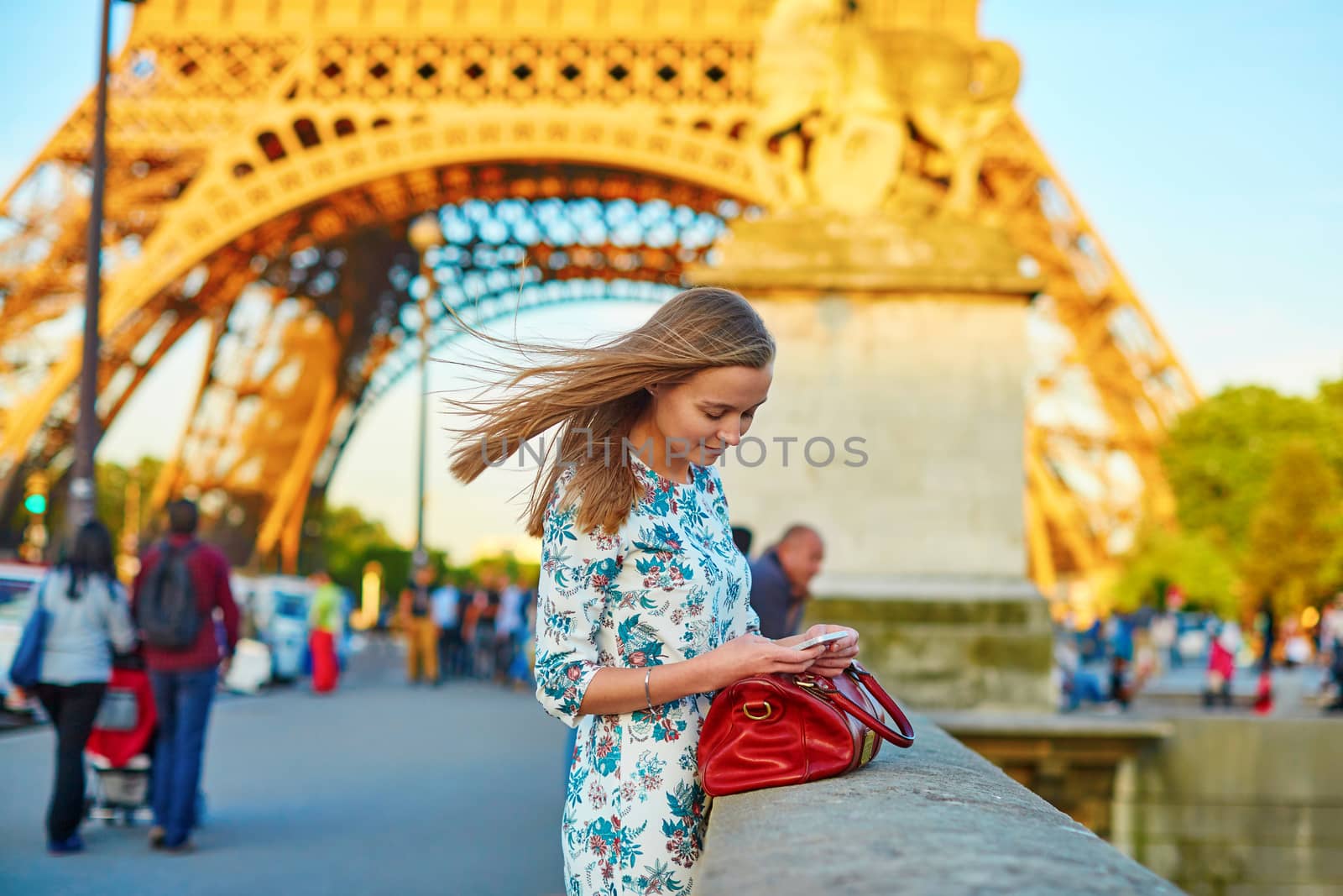 Young beautiful and elegant Parisian woman in blue dress near the Eiffel tower in Paris, checking her mobile phone