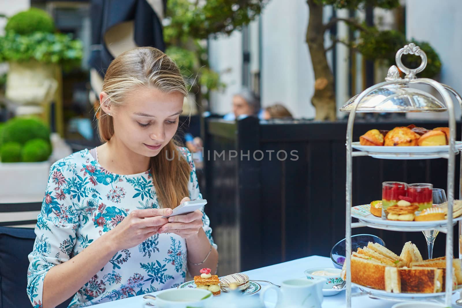 Beautiful young woman enjoying afternoon tea with selection of fancy cakes and sandwiches in a luxury Parisian restaurant