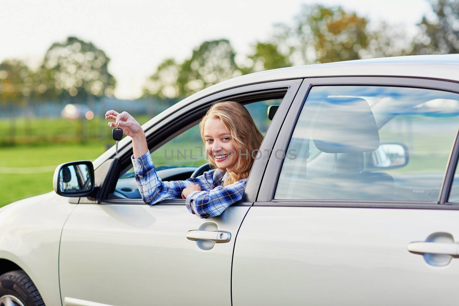 Beautiful young driver looking out of the car window holding a key