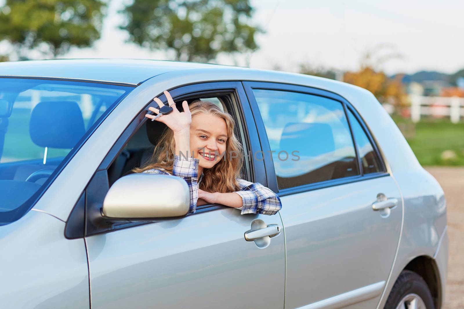 Beautiful young driver looking out of the car window holding a key