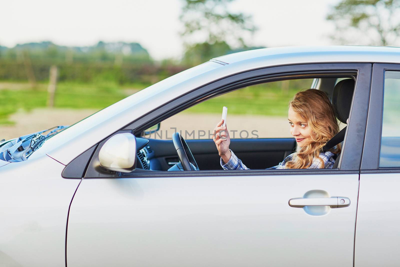 Young woman using her smartphone and making selfie while driving a car